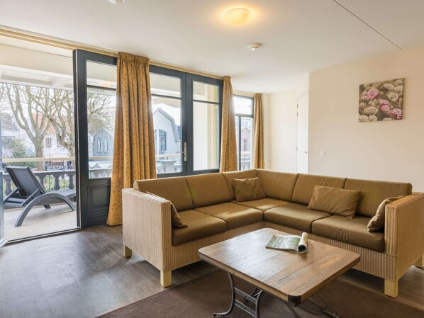 A living room with a sectional sofa, a wooden coffee table, and a view of the outside through large windows. - Apartment in Domburg Near the Beach (Domburg)