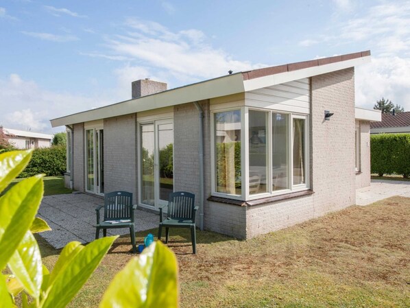 A modern single-story house with a patio area featuring two chairs and a table. - Bungalow in Netherlands With Private Sauna (Kamperland)