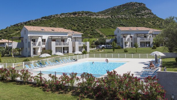 A hotel with a swimming pool, white buildings, and a mountain in the background. - Apartment in Corsica Near Beaches (Oletta)