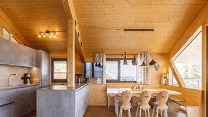 A modern kitchen with a central island, wooden cabinets, and a dining area with heart-shaped chairs. - Chalet With Panoramic Sauna (Schladming)