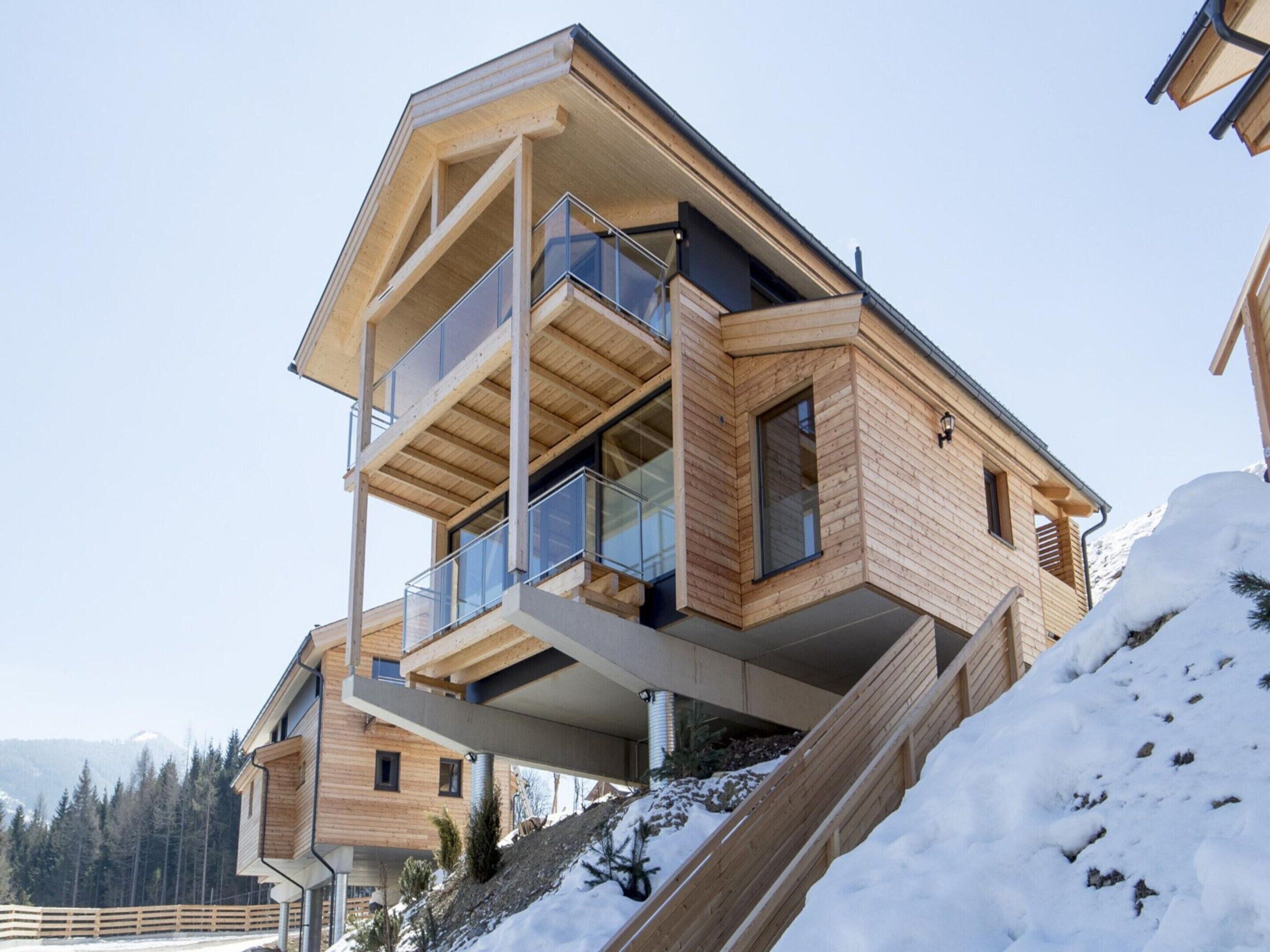 Un bâtiment moderne en bois, à plusieurs étages, doté de balcons, qui se dresse sur fond de montagnes enneigées.