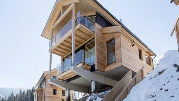 Un bâtiment moderne en bois, à plusieurs étages, doté de balcons, qui se dresse sur fond de montagnes enneigées.