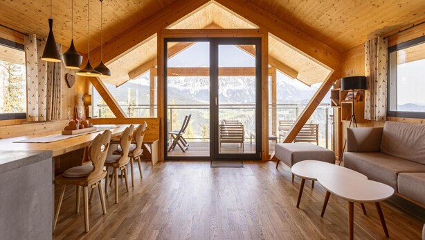 A spacious loft-style room with a wooden ceiling and floor, a large sliding glass door leading to a balcony with a mountain view, and a cozy seating area with a sofa and chairs. - Chalet With Panoramic Sauna (Schladming)