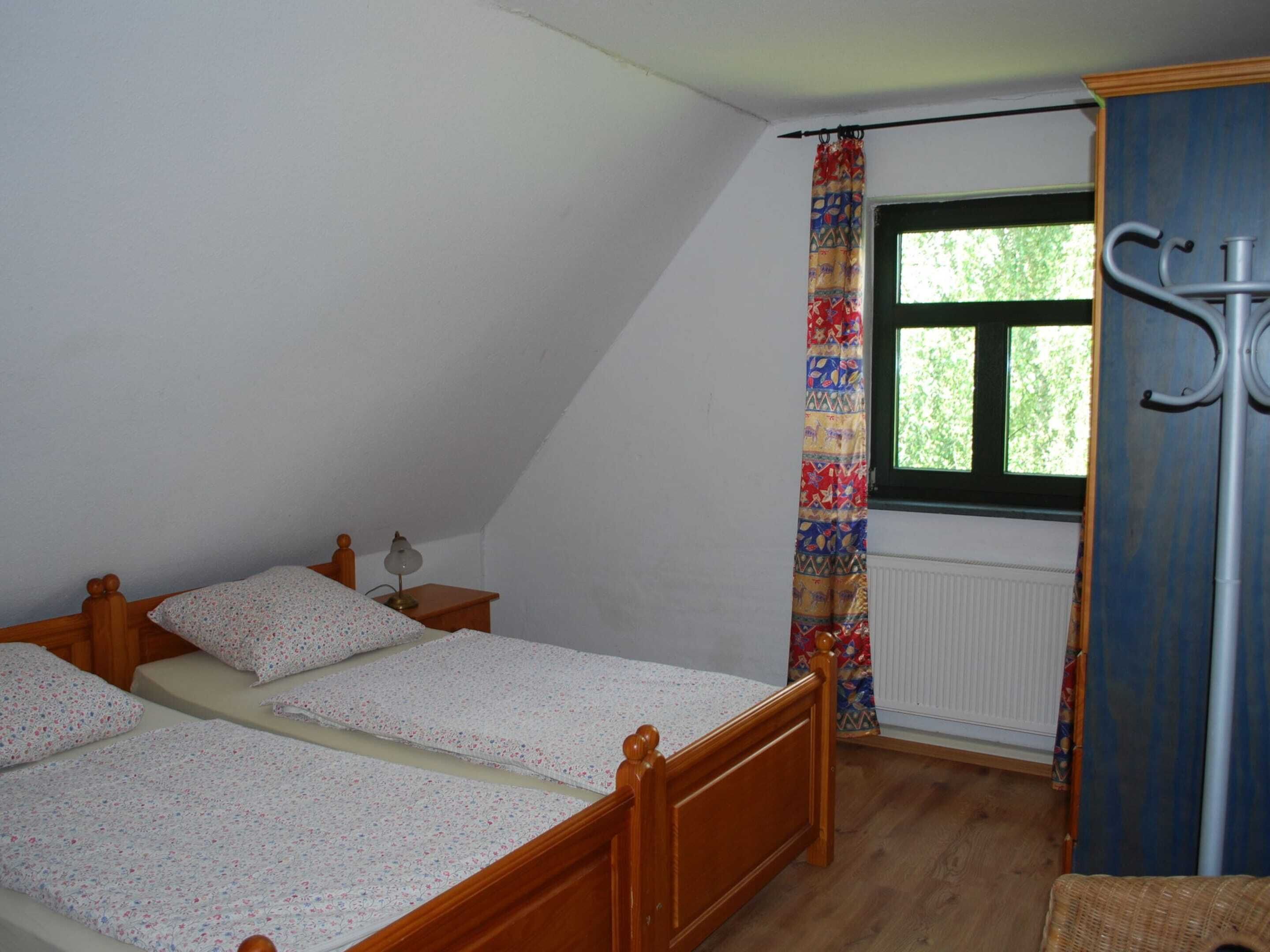 A bedroom with a sloped ceiling, a window with a curtain, a bed with floral bedding, a nightstand with a lamp, and a radiator.