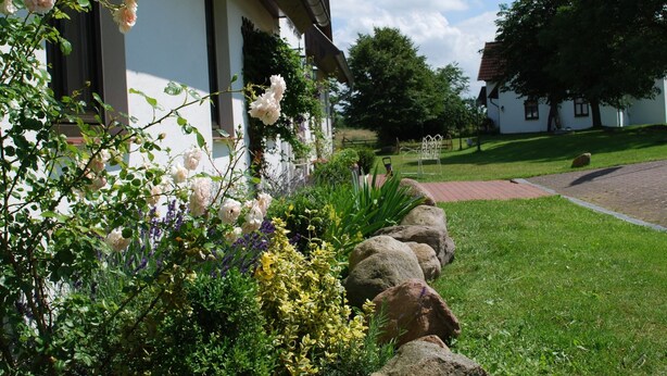 A building with a white facade, large windows, and a garden with flowers and shrubs. - Landhaus mit Schwimmbad in Dargun (Dargun)