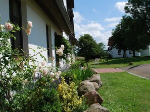 En bygning med hvid facade, store vinduer og en have med blomster og buske.