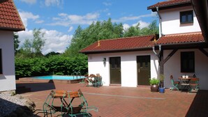 A courtyard with a swimming pool, outdoor seating, and a building with a red-tiled roof. - Landhaus mit Schwimmbad in Dargun (Dargun)