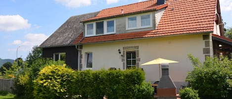A two-story house with a red-tiled roof, a chimney, and a small patio area with a yellow umbrella.