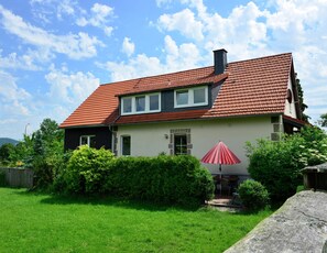 A two-story house with a red-tiled roof, a chimney, and a small garden with a red umbrella.