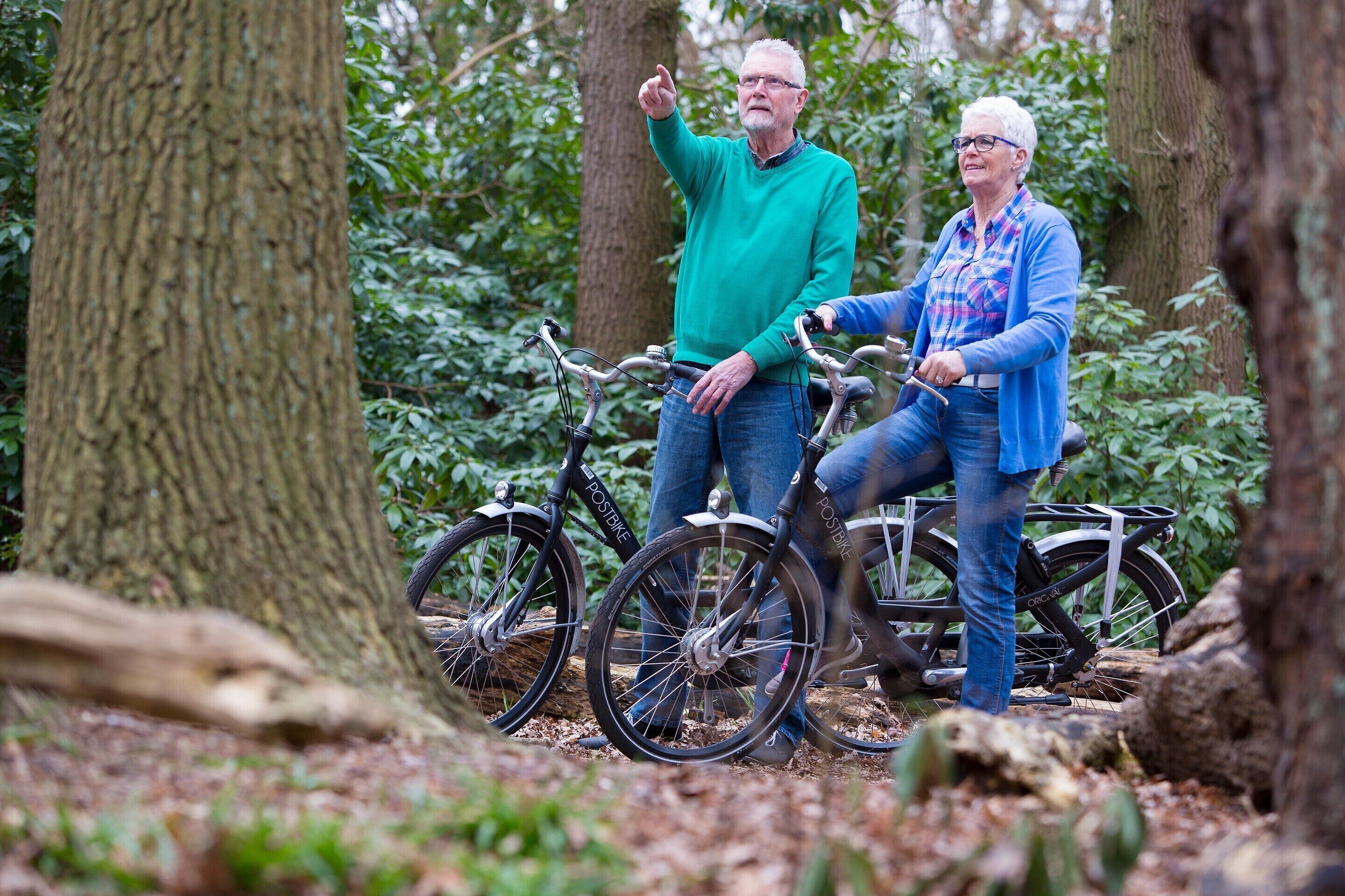 Two people standing next to bicycles in a forested area.