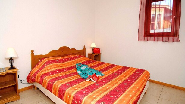 A bedroom with a wooden bed, two bedside tables, a window with a red curtain, and a lamp on each table. - Chalet in France Near Ski Slopes (Le Dévoluy)