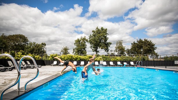 Una piscina con acqua cristallina, circondata da lettini e una recinzione.
