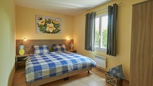 Un dormitorio con cama, dos mesitas de noche, una lámpara de pared, una ventana con cortinas y un cuadro en la pared.