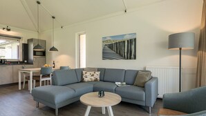 Ein modernes Wohnzimmer mit einem grauen Ecksofa, einem runden Couchtisch und einem Essbereich mit weißem Tisch und Stühlen.