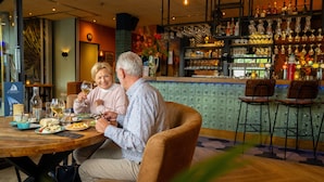 Un couple est assis à une table dans un restaurant, avec un bar visible à l'arrière-plan.