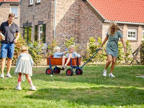 A family with a child in a wagon, a house with a red roof, and a brick exterior. - Nice Villa With Sauna, Whirlpool & Steam Shower (Roggel)