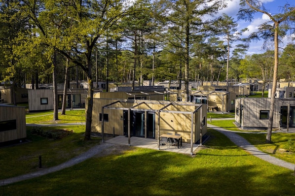 Un terrain de camping doté de plusieurs chalets de type caravane, d’un bâtiment central avec un patio couvert et d’une grande pelouse bien entretenue.