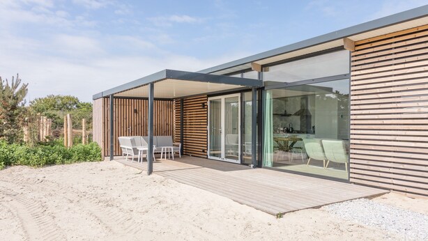 Une maison de plage moderne dotée d’une terrasse en bois, de portes coulissantes en verre et d’un espace patio.