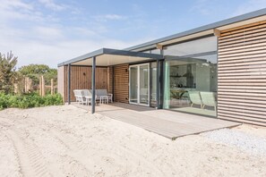 Une maison de plage moderne dotée d’une terrasse en bois, de portes coulissantes en verre et d’un espace patio.