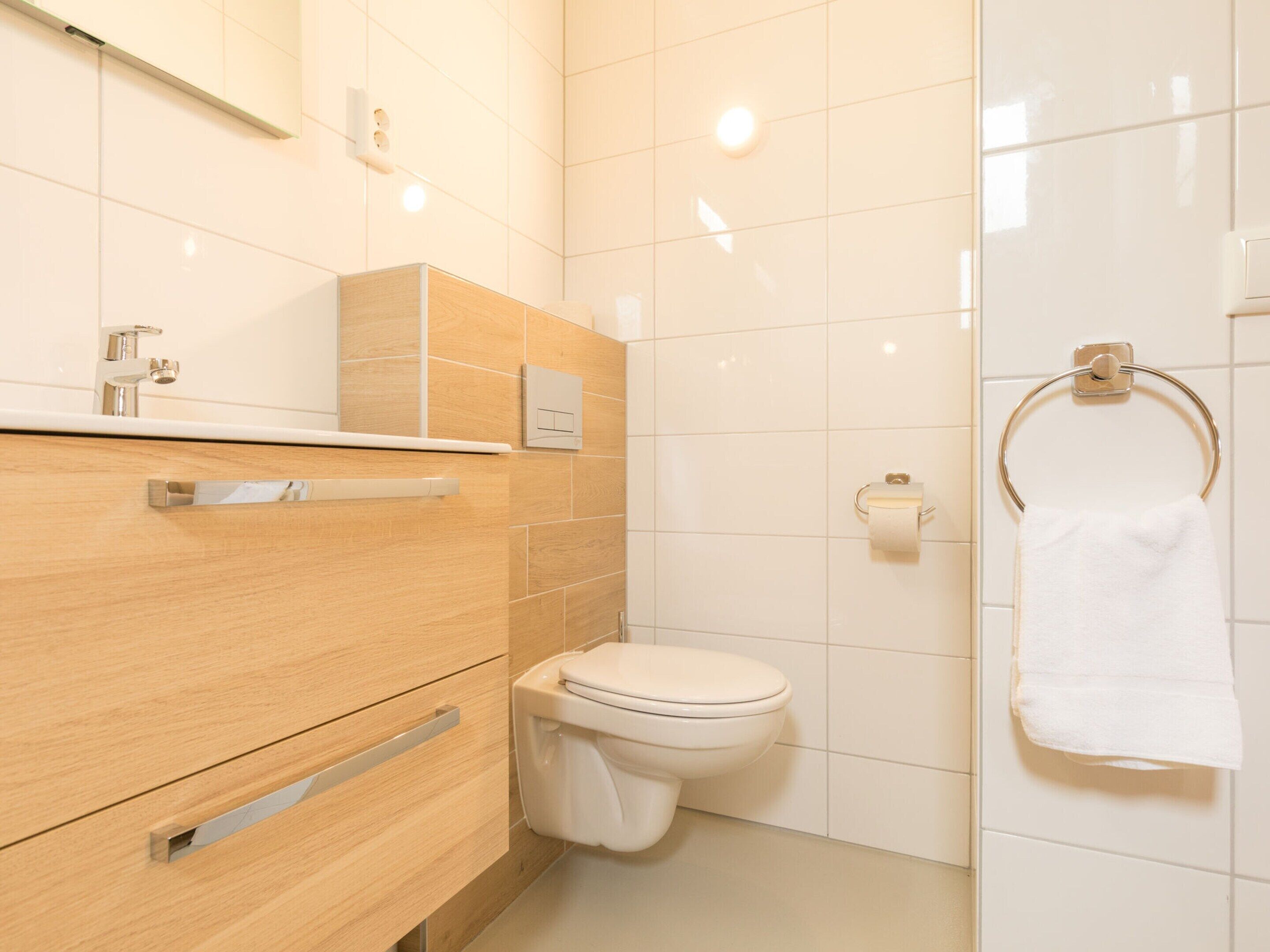 A modern bathroom with a wooden vanity, a white toilet, and a towel ring.