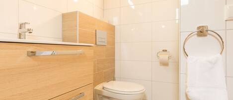 A modern bathroom with a wooden vanity, a white toilet, and a towel ring.