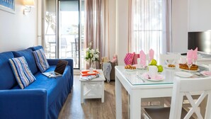 A modern living room with a blue sofa, a dining table set with plates, glasses, and a laptop. - Apartment in Cote D'amour by La Baule Bay (Pornichet)