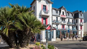 A multi-story building with balconies, a red awning, and palm trees in the foreground. - Apartment in Cote D'amour by La Baule Bay (Pornichet)