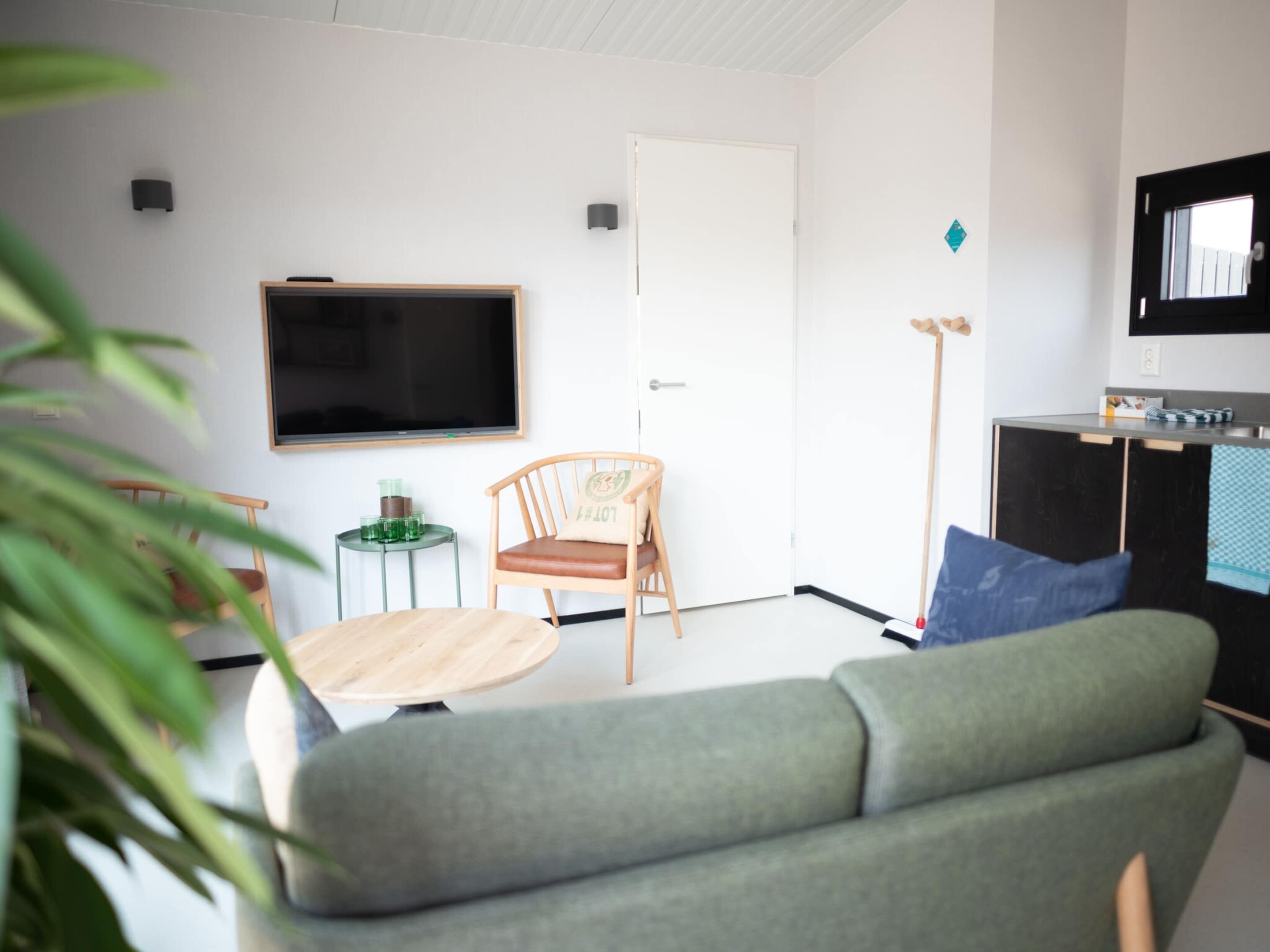A living room with a green sofa, a wooden chair, a small round table, a television, and a door.