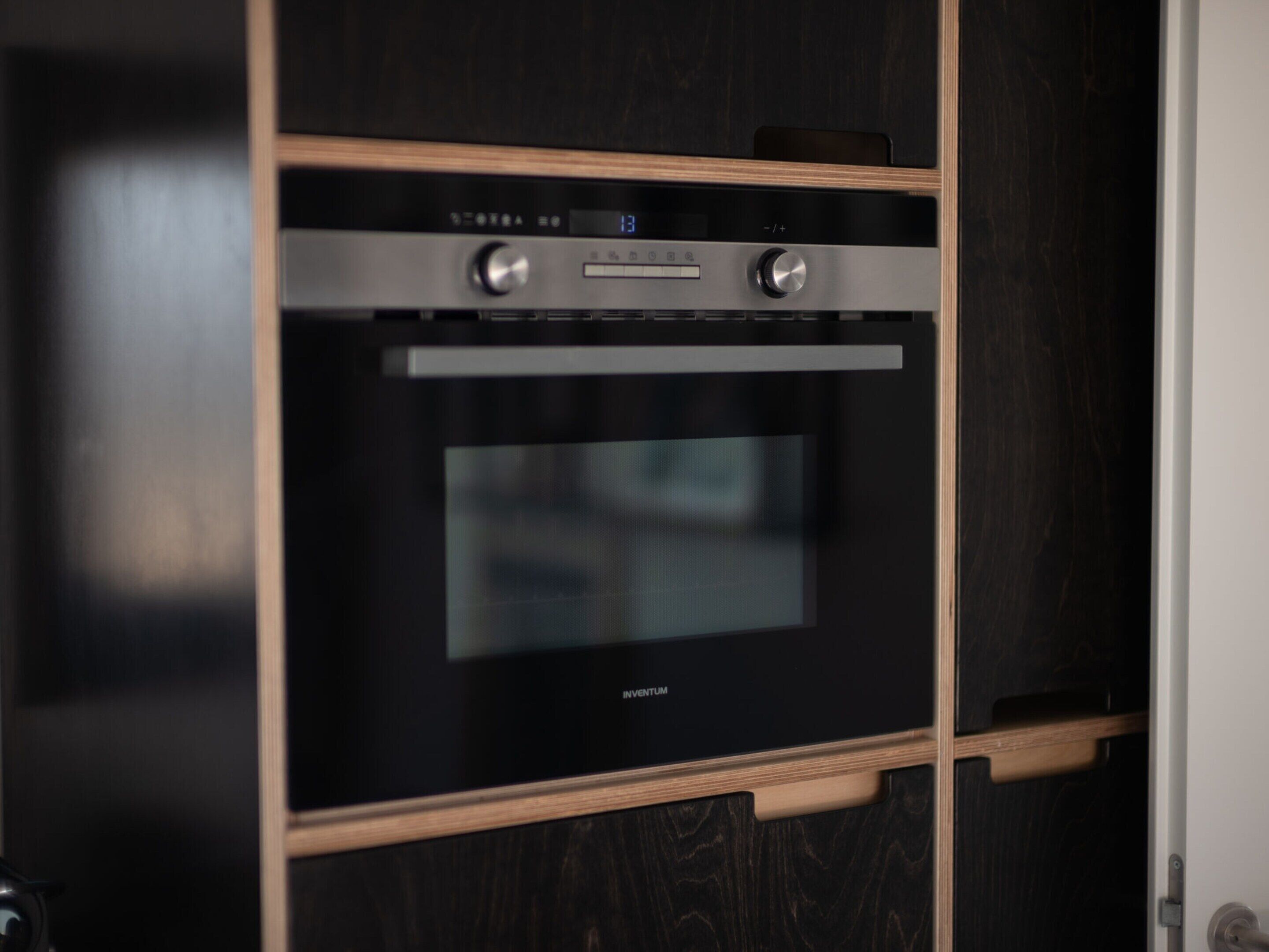 Cocina moderna con horno integrado y microondas, con un acabado elegante en negro y muebles de madera.