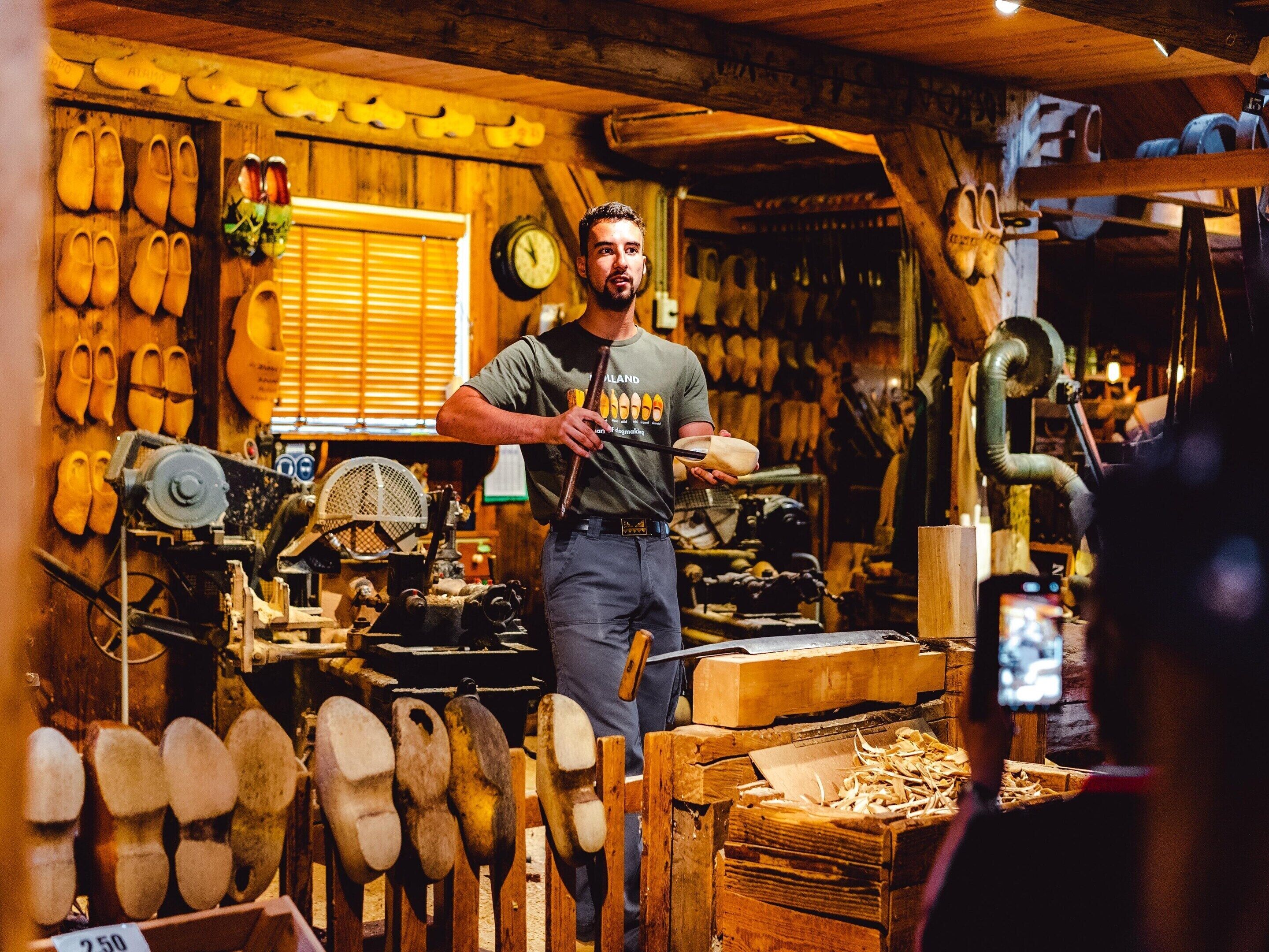 A workshop with wooden shoes and tools, a clock on the wall, and a person holding a shoe.