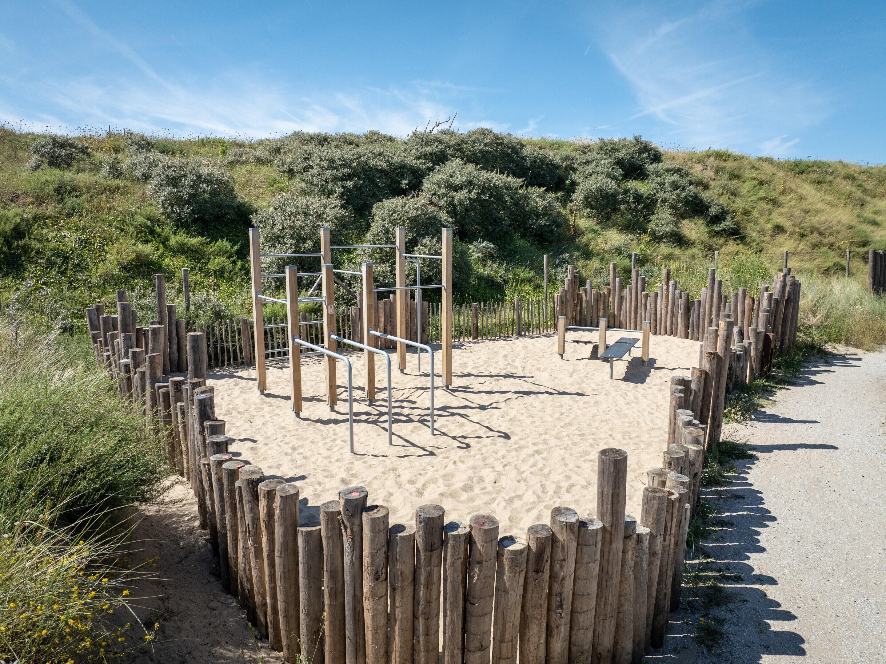 A sandy outdoor area with a wooden fence and metal climbing structures.