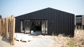 A modern building with a black exterior, large glass doors, and a seating area with white chairs.
