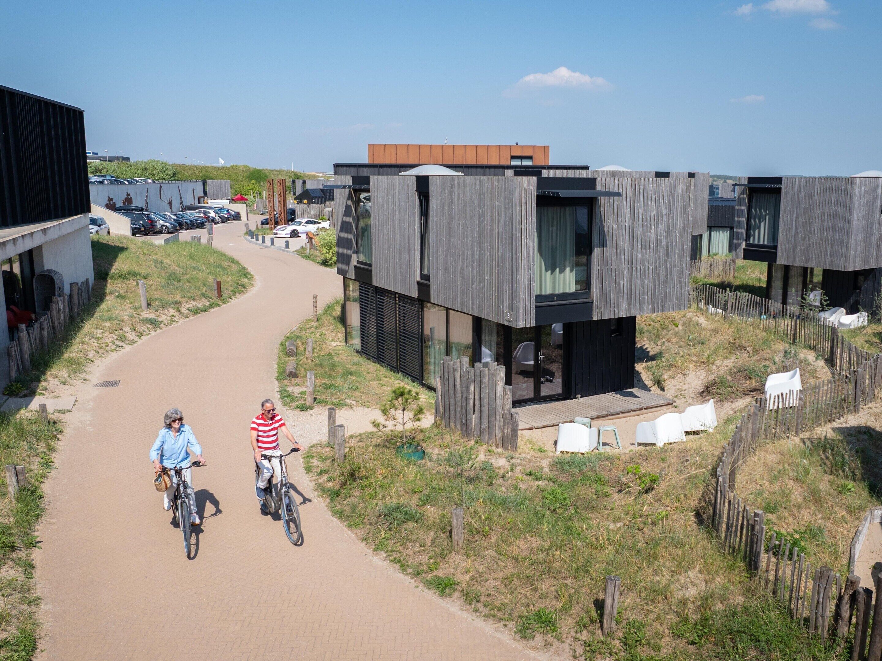 A modern building with a wooden facade, a paved pathway, and a grassy area with a fence.