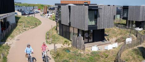 A modern building with a wooden facade, a paved pathway, and a grassy area with a fence.