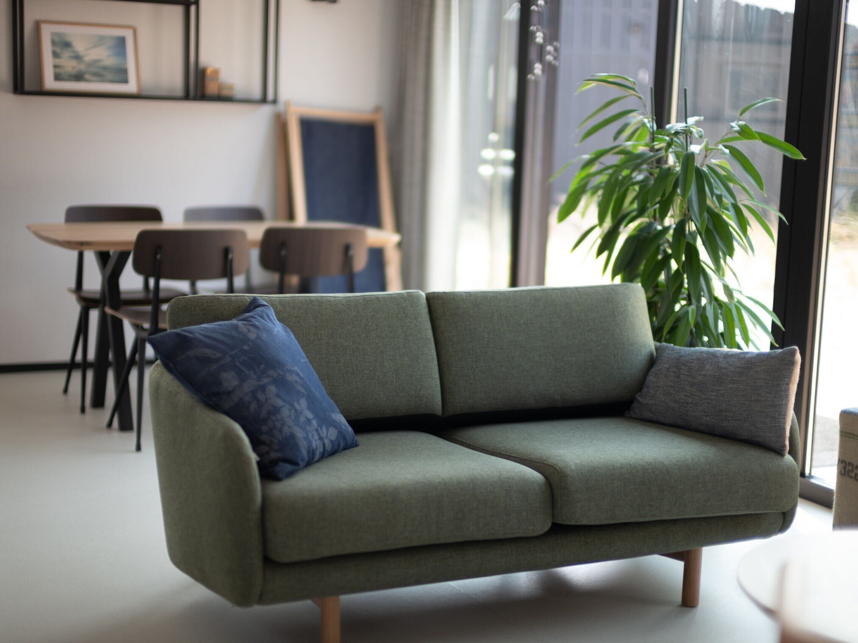 Ein stilvolles Wohnzimmer mit einem grünen Sofa, zwei Sesseln, einem Esstisch und einer großen Pflanze.