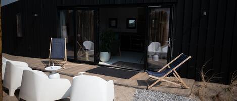 Un espace extérieur moderne aménagé avec des chaises blanches et un hamac, une porte-fenêtre et une plante en pot à l’intérieur.