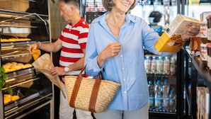 Een buffetgedeelte, met een man in een gestreepte shirt die eten serveert en een vrouw in een blauwe shirt een doos cornflakes vasthoudt.