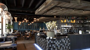 Un interno ristorante moderno con zona bar, travi in legno a soffitto e un'ampia pianta in vaso.