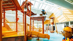 Area giochi acquatici interna con scivoli e giochi d'acqua, circondata da strutture e ringhiere in legno.