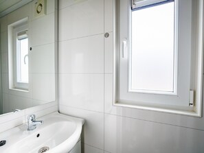 A bathroom with a white sink, mirror, and window. - Beautiful Lodge at the Lake and Beach (Maurik)