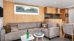 A modern living room with a grey sofa, a small white table with a bottle and glasses, and a wooden cabinet with a window above. - Cozy Chalet w/ Shared Pool (Borger)