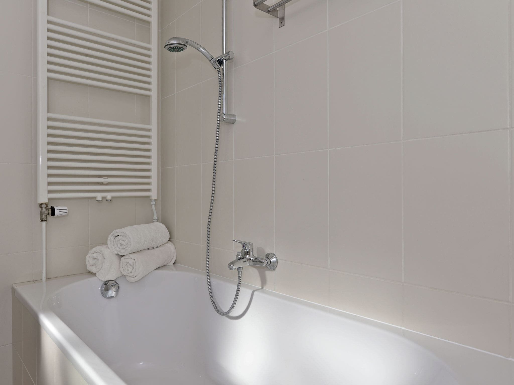 A modern bathroom with a white bathtub, a handheld showerhead, and a towel rack with folded towels.