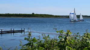 A calm lake with sailboats, a wooden dock, and lush greenery in the foreground. - Bungalow Near Veerse Meer & Beach (Kamperland)