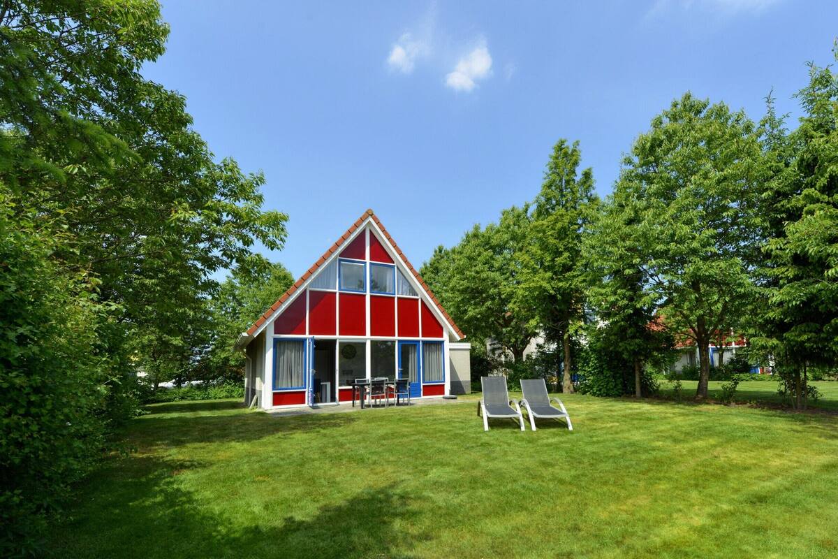Un edificio rojo y blanco con techo triangular, rodeado de césped y árboles verdes.