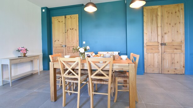 A dining area with a wooden table and chairs, a vase with flowers, and two pendant lights. - Castle in Asnieres With Tennis & Forest Views (Asnieres)