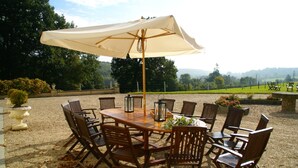 An outdoor patio with a wooden table and chairs, a large umbrella, and a view of a green landscape. - Castle in Asnieres With Tennis & Forest Views (Asnieres)