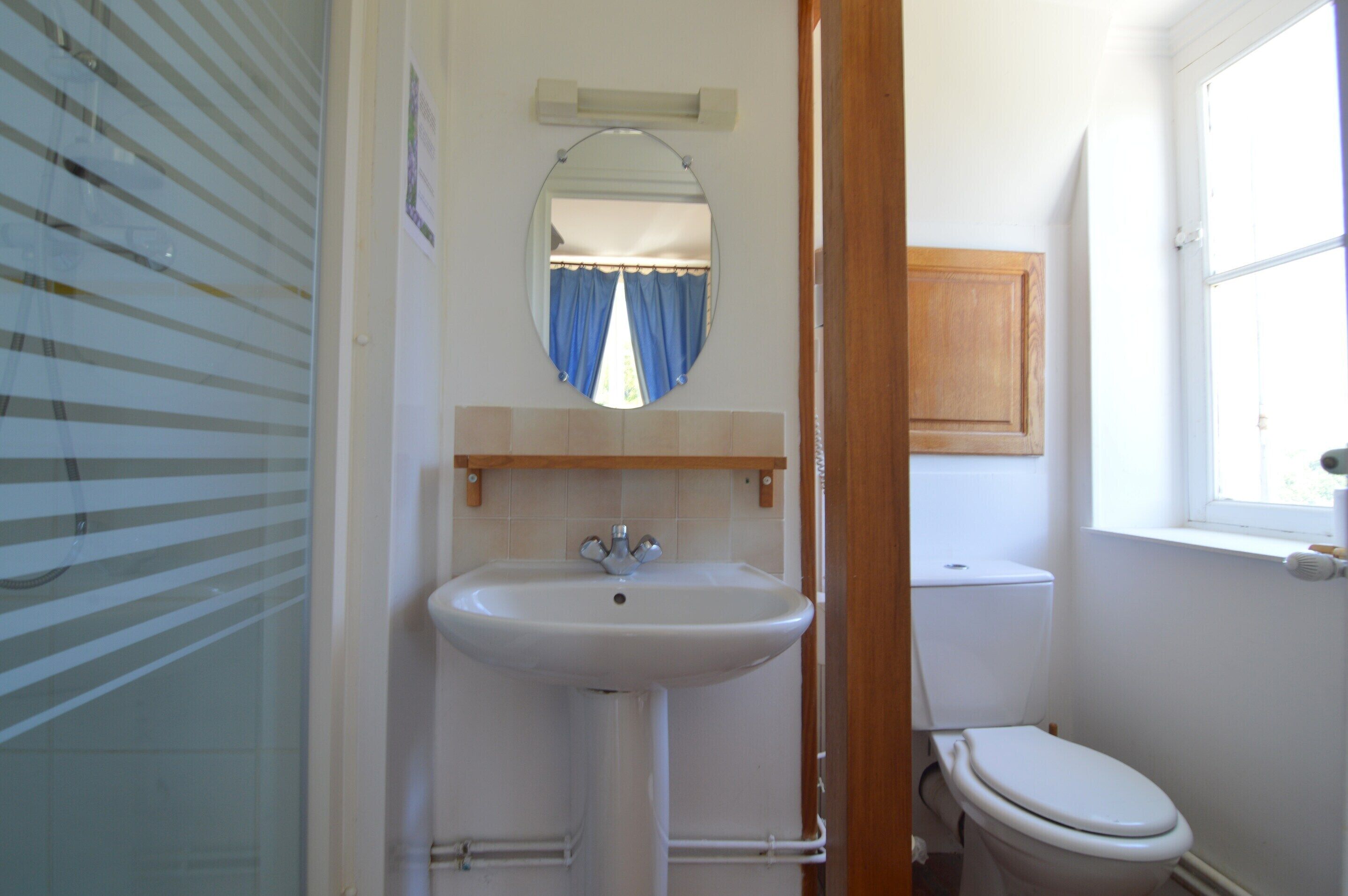 A bathroom with a sink, mirror, toilet, and a window.