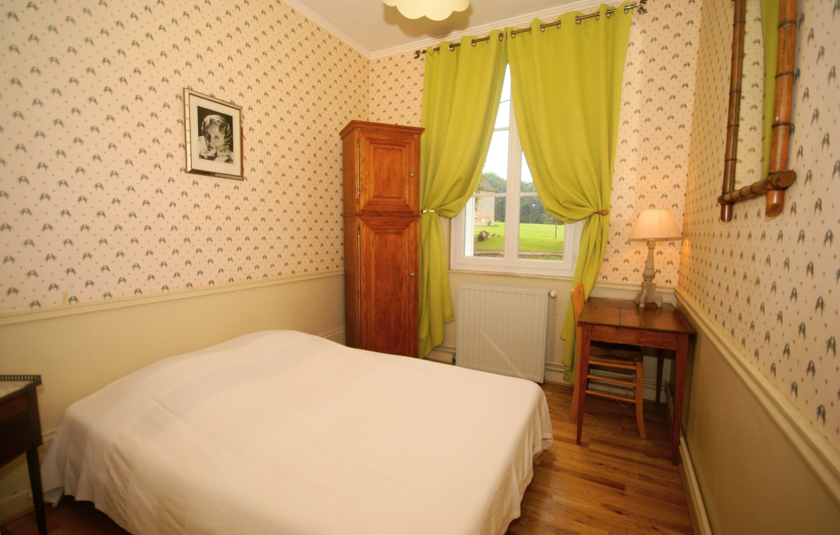 Une chambre à coucher avec un lit, une armoire en bois, une fenêtre avec des rideaux verts et une lampe sur une table.