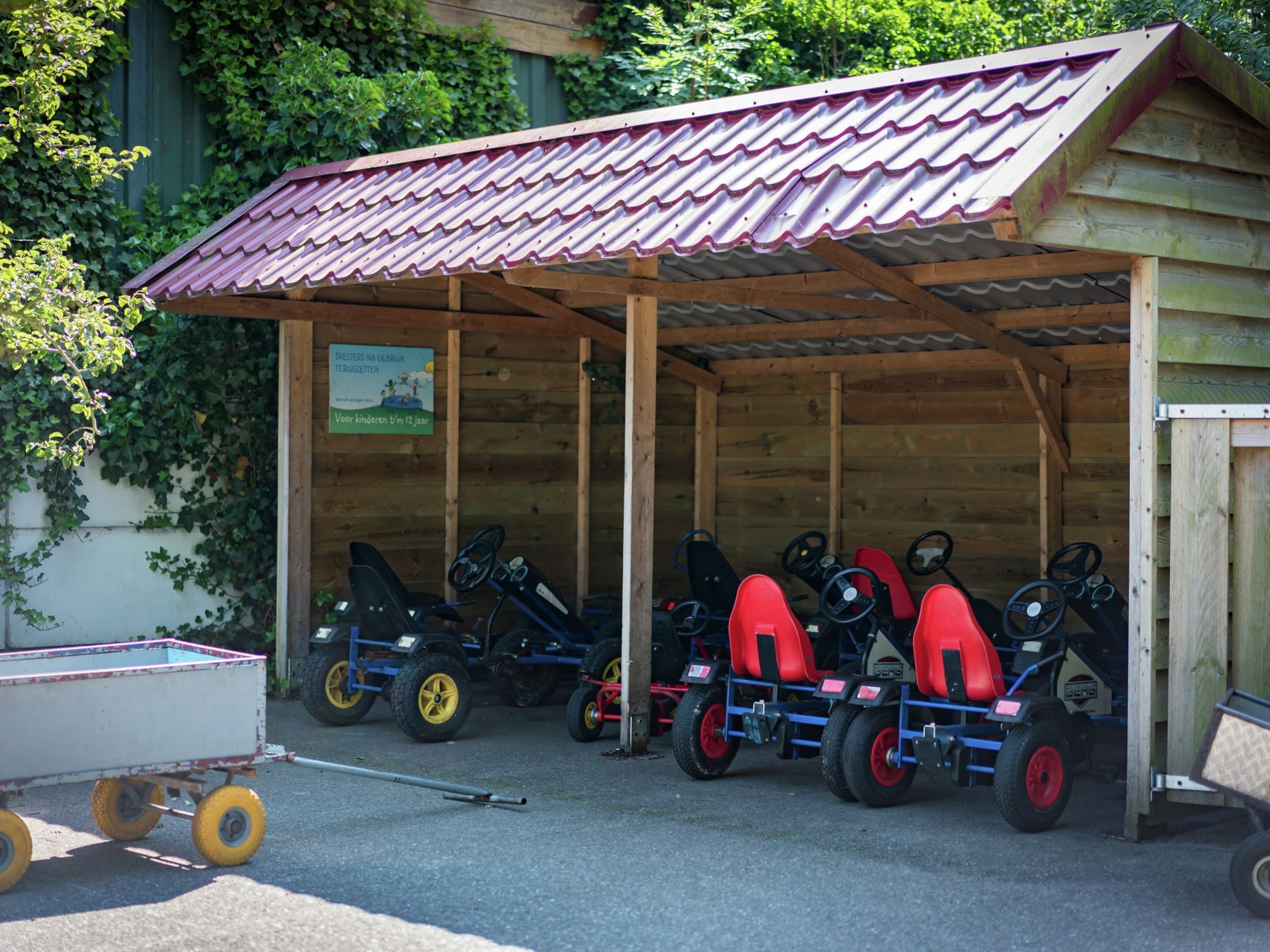 Ein überdachter Außenbereich mit einer Holzkonstruktion, in der mehrere kleine Spielzeugautos in Rot und Schwarz ausgestellt sind.