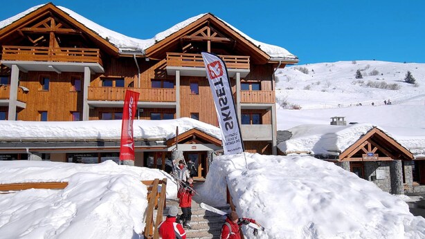 A wooden lodge with multiple balconies, a reception area, and ski equipment in the foreground. - Family & Pet-friendly Base (Valmeinier)